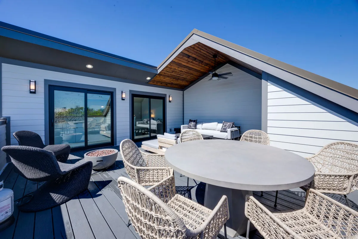 An inviting exterior space featuring a dining table, comfortable seating, and a fire pit, all within a fenced area that suggests a communal yard. The setting is relaxed and perfect for outdoor gatherings or playtime in a secure environment.