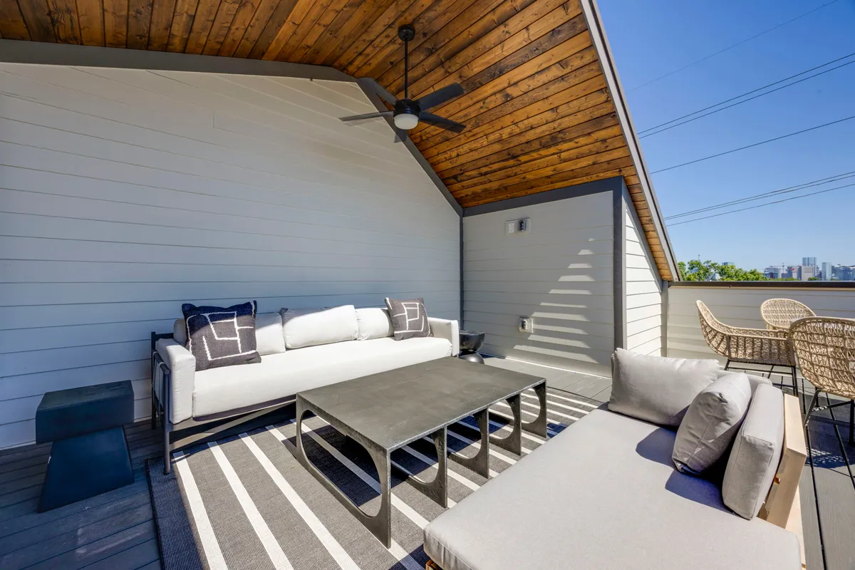 An outdoor lounge area with a sofa, woven chairs, coffee table, and a ceiling fan, set in a relaxed environment. The space encourages both socializing and quiet moments, with a sense of openness suited to pets and their owners.