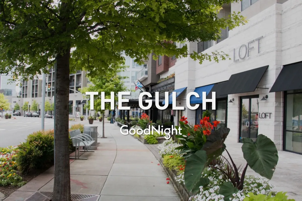 A vibrant street scene with storefronts, flower beds, and street trees, capturing the spirit of a walkable, lively neighborhood with outdoor dining and shopping opportunities.