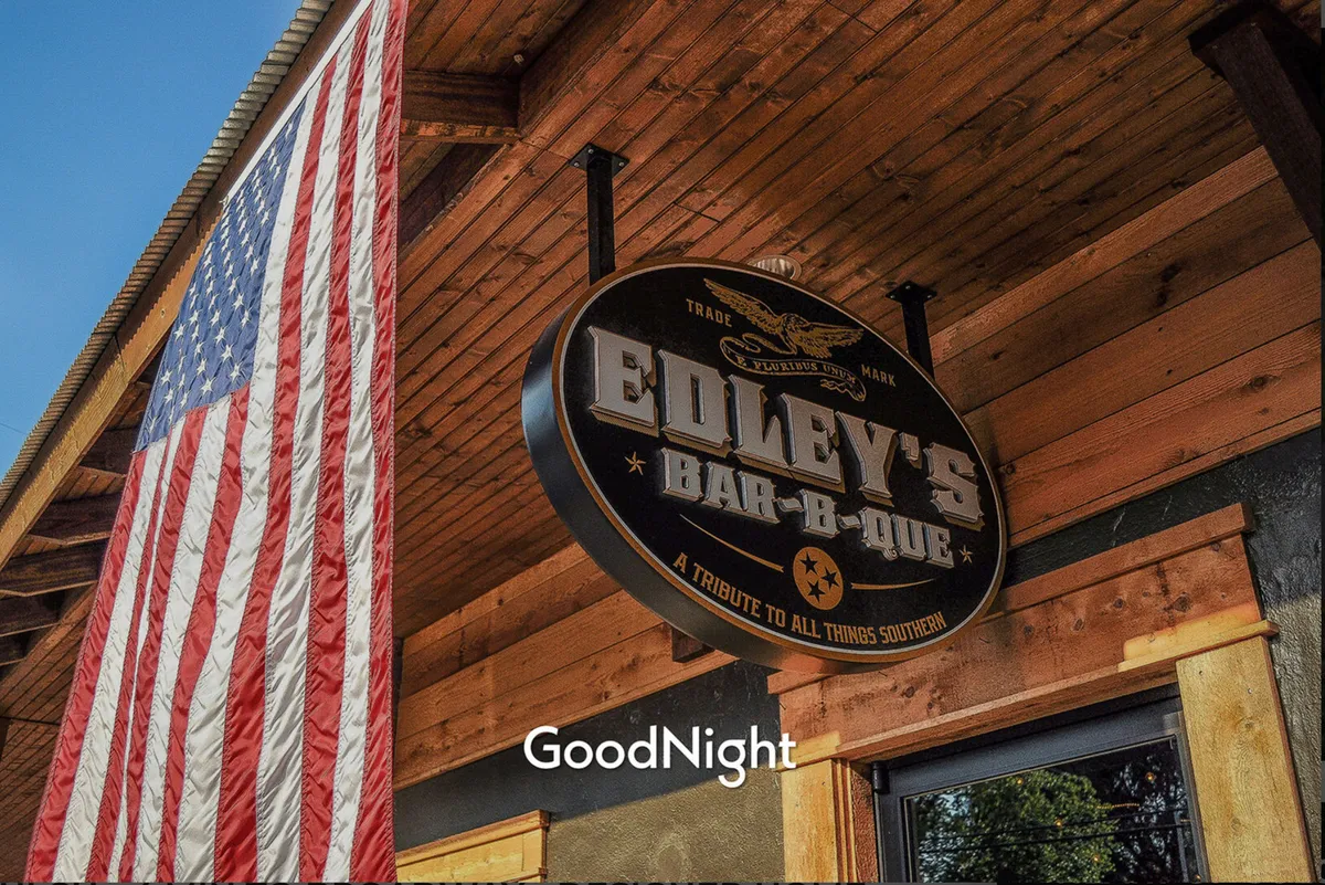 An exterior shot of Edley's Bar-B-Que, featuring the recognizable sign and American flag. The ambiance is lively and welcoming, with visible seating and a sense of community as people gather near the entrance. This image captures the Southern culinary spirit of Nashville.