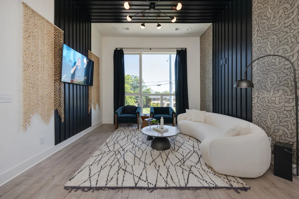 A bright, contemporary living room with a curved white sofa, round coffee table, black accent wall, large window, and decorative wall art. The space is open and inviting, filled with natural light, and features both a cozy seating arrangement and a sleek, modern style.