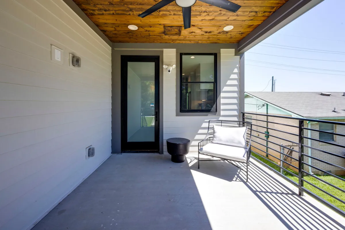 This image displays a welcoming front door with outdoor seating and a ceiling fan, set against a calm and inviting backdrop. The comfortable arrangement and greenery suggest a place where guests and pets alike can easily transition from inside to outside.
