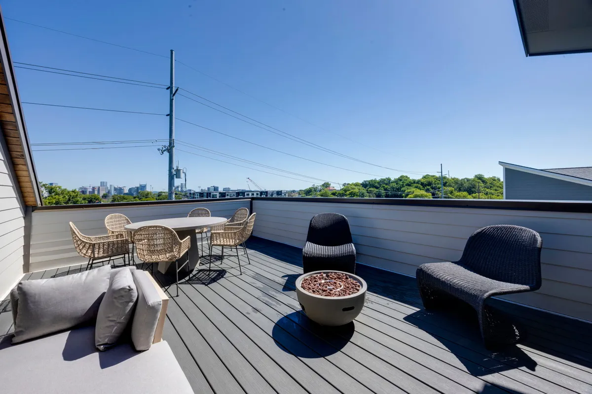 This exterior image shows a spacious outdoor seating area with a fire pit, surrounded by comfortable chairs, and a city skyline in the background. The atmosphere is inviting and relaxed, perfect for group gatherings, evening conversations, or enjoying the sunset together.