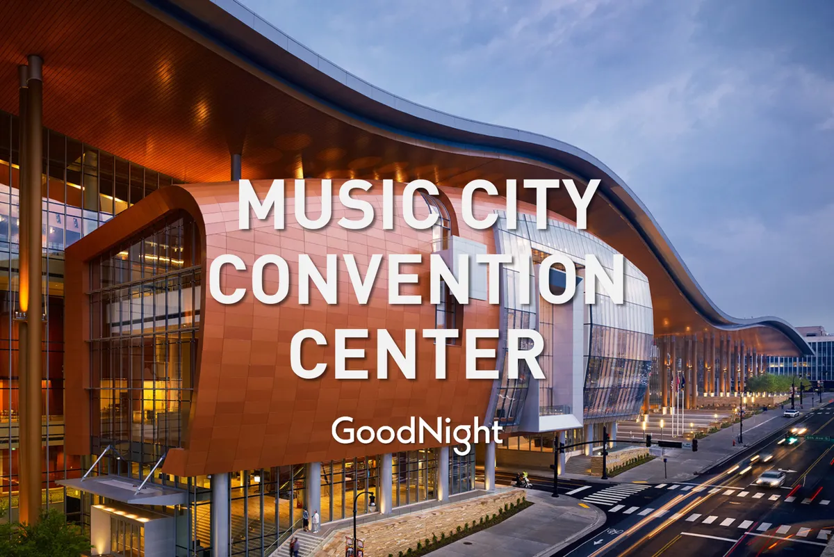 The exterior of the Music City Center, a prominent Nashville event venue, with its sweeping roof design, vibrant orange facade, and bustling street scene in the foreground. The glass panels reflect the sky, emphasizing the modern, dynamic atmosphere of the area.