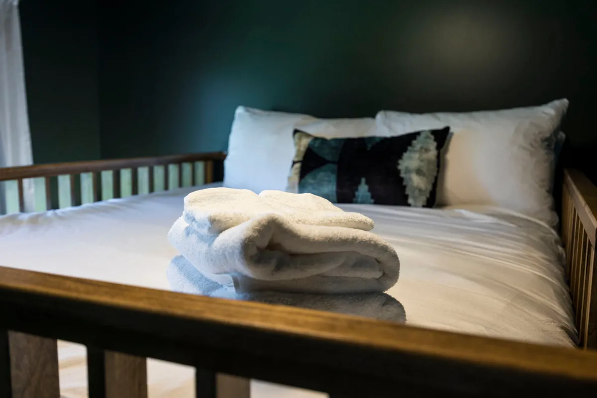 A serene bedroom featuring a well-made bed with a folded blanket and decorative pillow. Soft sunlight gently filters through the window, creating a tranquil atmosphere ideal for relaxation or reading. The space feels private and inviting.