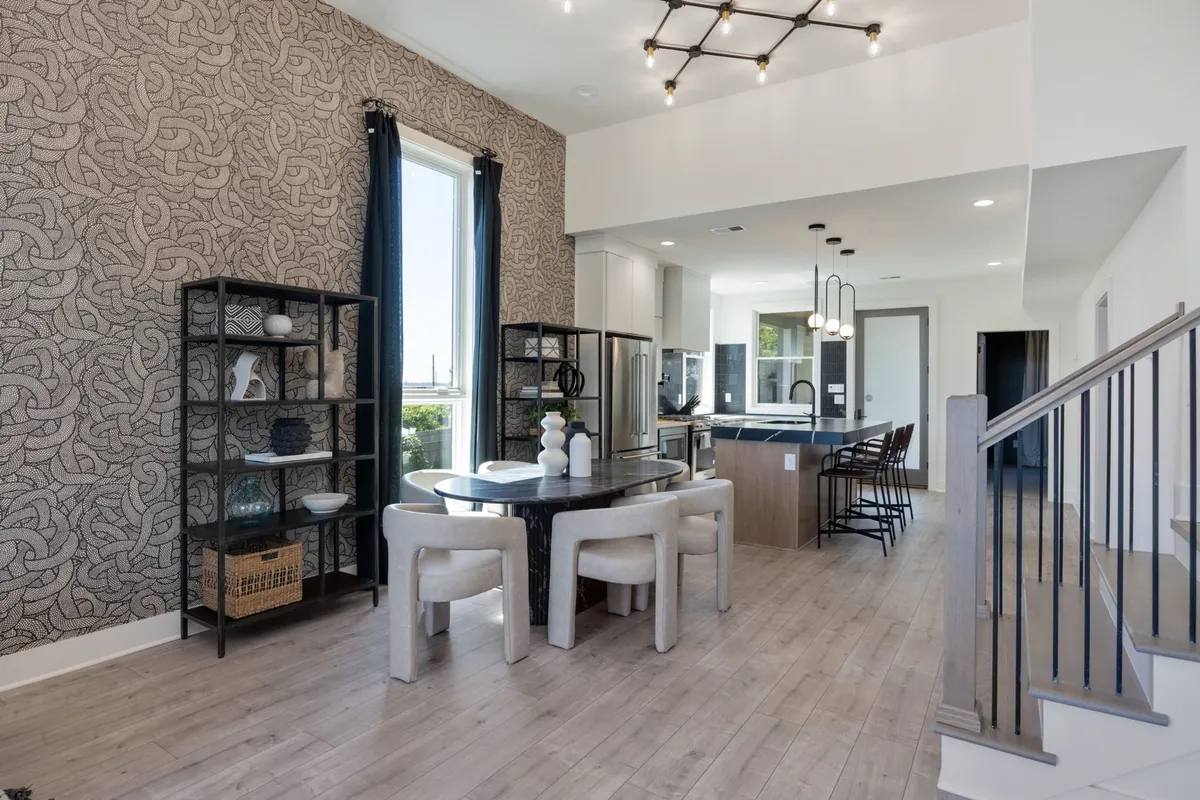 A stylish open-concept space combining a dining area and a kitchen with a central island, decorative shelving, and abundant natural light. The dining table is set for gatherings, while the kitchen is ready for meal prep, creating a seamless flow between dining and cooking.