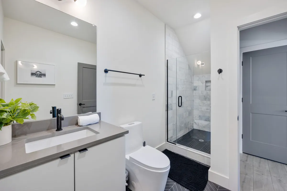 A refreshing, spa-inspired bathroom with a modern vanity, glass shower enclosure, and framed artwork. Morning sunlight pours through the window, emphasizing sparkling cleanliness and inviting amenities.